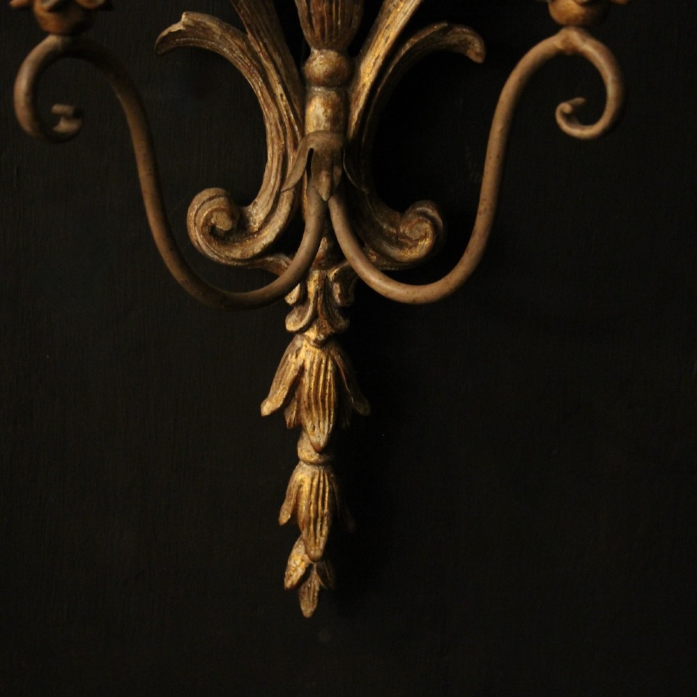 A pair of French carved wooden two-arm wall sconces featuring ornate floral basket motifs, acanthus leaf scrollwork, and white candle sleeves. View IX