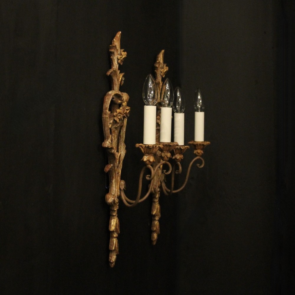 A pair of French carved wooden two-arm wall sconces featuring ornate floral basket motifs, acanthus leaf scrollwork, and white candle sleeves. View X