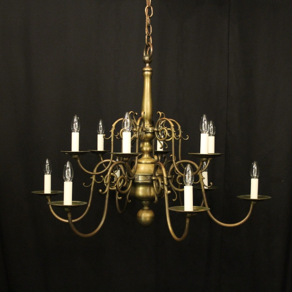 An antique English twelve-light bronze chandelier featuring scrollwork arms, candle sleeves, drip pans, and a turned central stem.