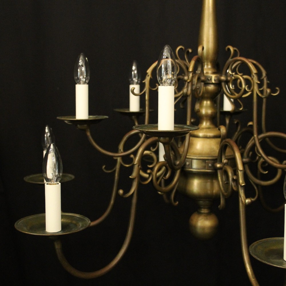 An antique English twelve-light bronze chandelier featuring scrollwork arms, candle sleeves, drip pans, and a turned central stem. View II