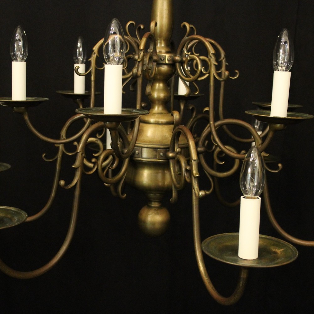 An antique English twelve-light bronze chandelier featuring scrollwork arms, candle sleeves, drip pans, and a turned central stem. View III