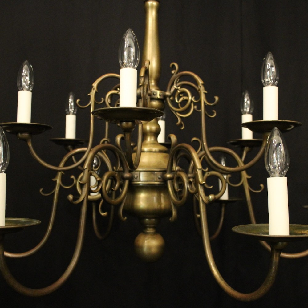 An antique English twelve-light bronze chandelier featuring scrollwork arms, candle sleeves, drip pans, and a turned central stem. View V