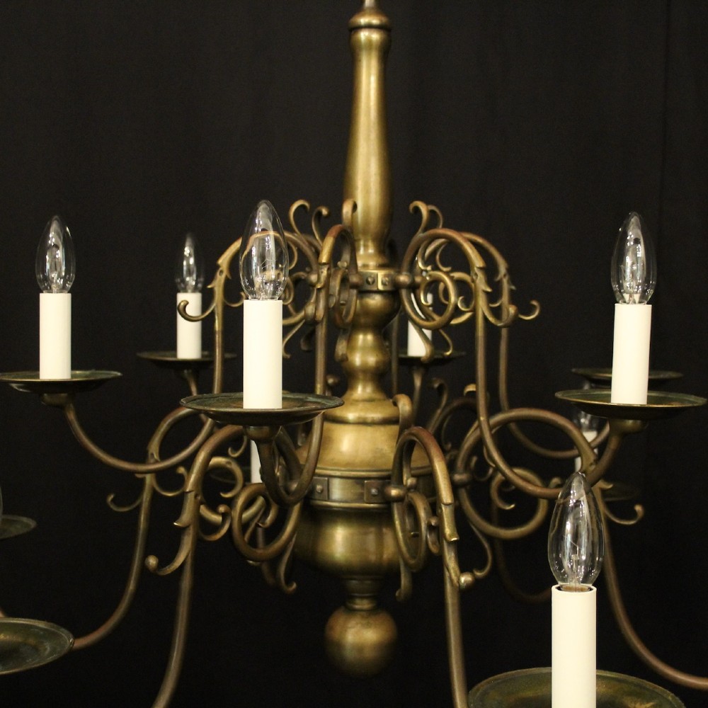 An antique English twelve-light bronze chandelier featuring scrollwork arms, candle sleeves, drip pans, and a turned central stem. View VII
