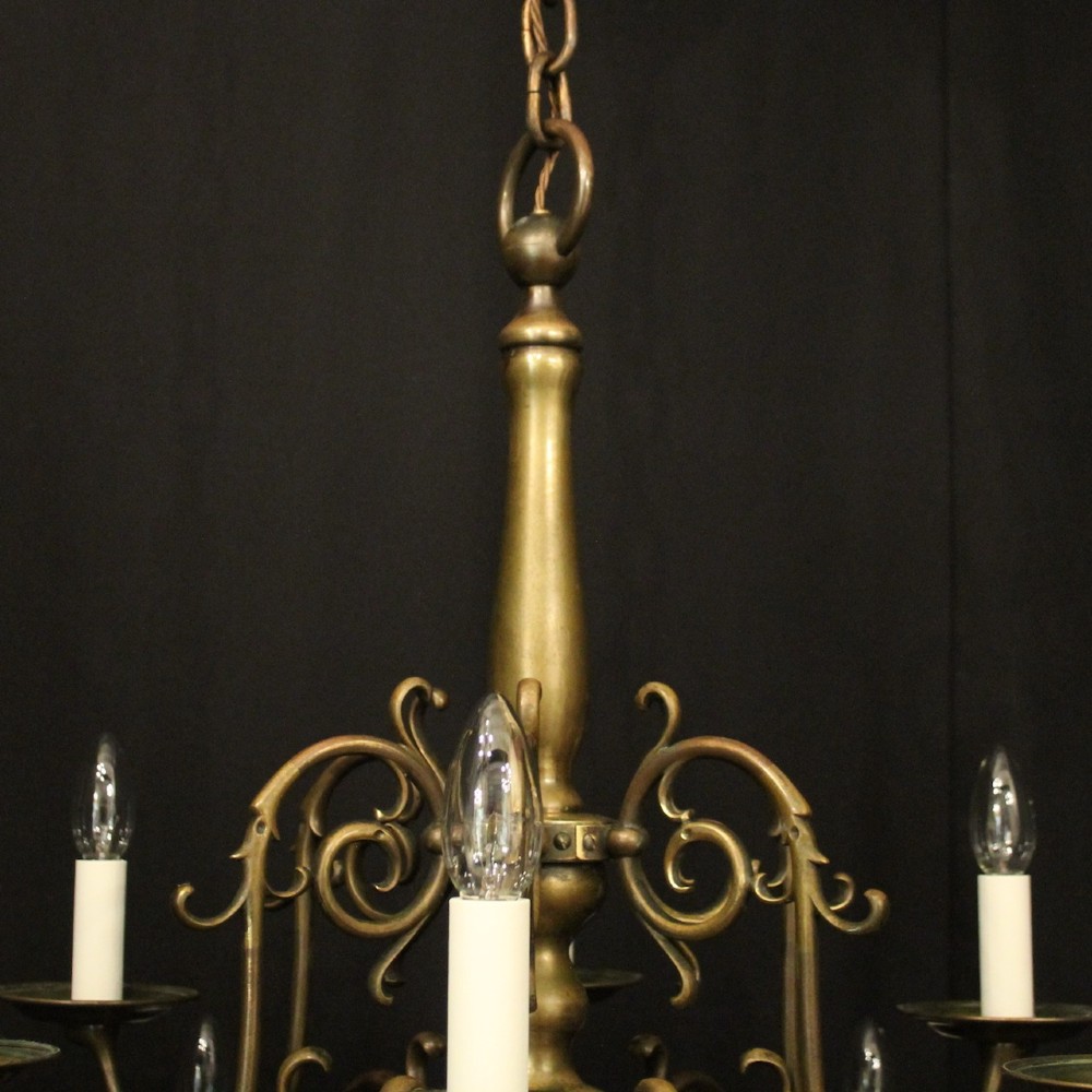 An antique English twelve-light bronze chandelier featuring scrollwork arms, candle sleeves, drip pans, and a turned central stem. View IX