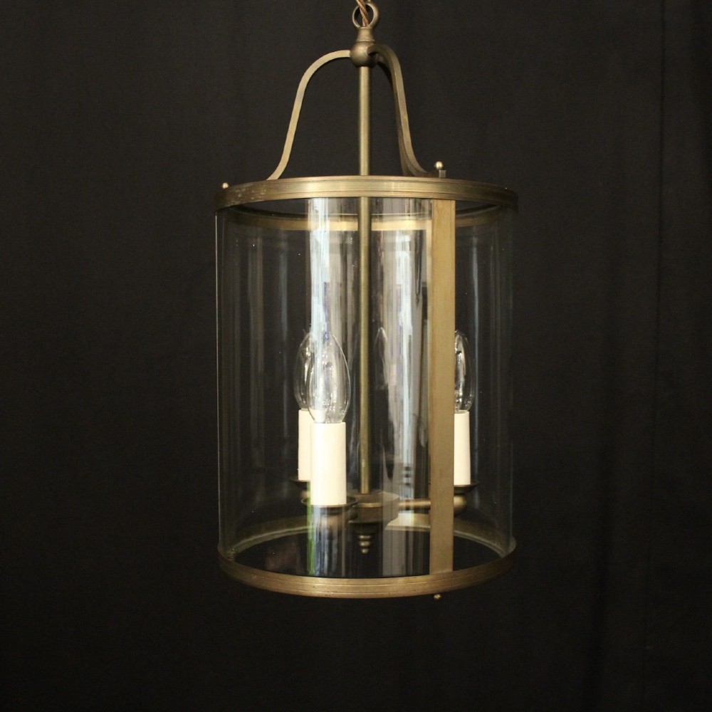 A cylindrical gilt brass hall lantern featuring curved clear glass panels, a central three-light candle fixture, and a suspended hanging chain. View II