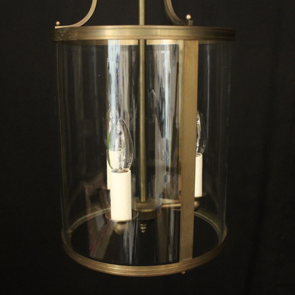 A cylindrical gilt brass hall lantern featuring curved clear glass panels, a central three-light candle fixture, and a suspended hanging chain. View VI
