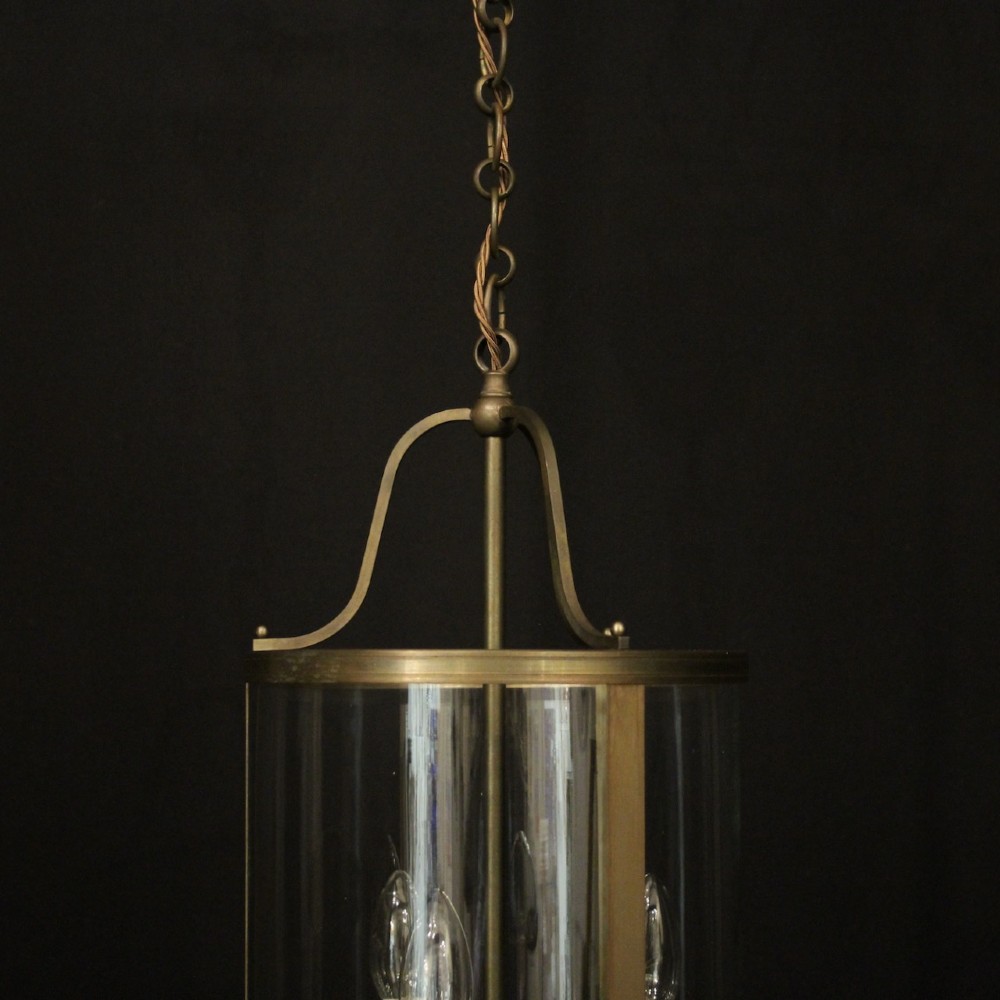 A cylindrical gilt brass hall lantern featuring curved clear glass panels, a central three-light candle fixture, and a suspended hanging chain. View VIII