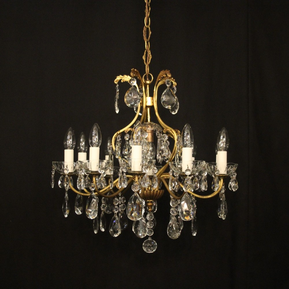 A nine-light French gilded metal chandelier featuring curved scroll arms, white candle sleeves, and suspended clear glass droplet pendants.