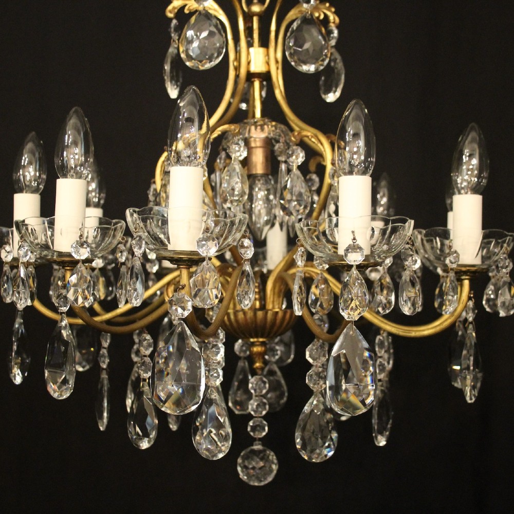 A nine-light French gilded metal chandelier featuring curved scroll arms, white candle sleeves, and suspended clear glass droplet pendants. View II