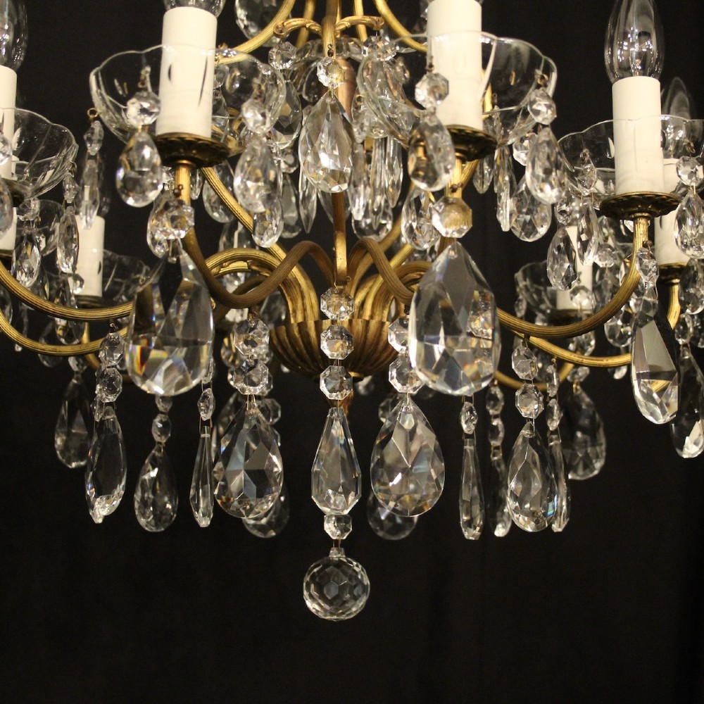 A nine-light French gilded metal chandelier featuring curved scroll arms, white candle sleeves, and suspended clear glass droplet pendants. View IV
