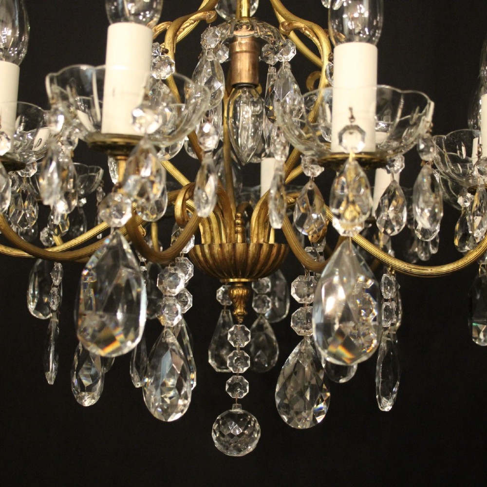 A nine-light French gilded metal chandelier featuring curved scroll arms, white candle sleeves, and suspended clear glass droplet pendants. View V