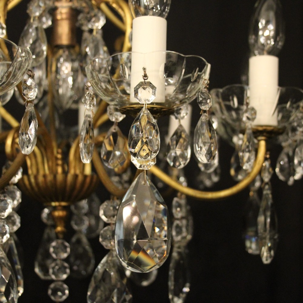 A nine-light French gilded metal chandelier featuring curved scroll arms, white candle sleeves, and suspended clear glass droplet pendants. View VI