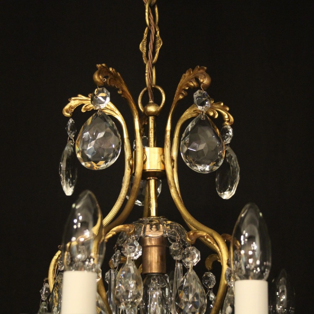 A nine-light French gilded metal chandelier featuring curved scroll arms, white candle sleeves, and suspended clear glass droplet pendants. View VII