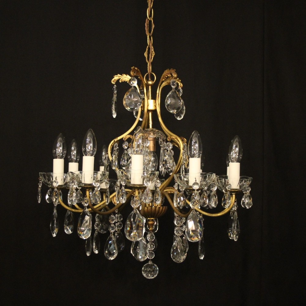 A nine-light French gilded metal chandelier featuring curved scroll arms, white candle sleeves, and suspended clear glass droplet pendants. View VIII