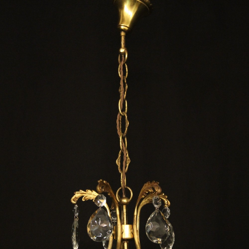 A nine-light French gilded metal chandelier featuring curved scroll arms, white candle sleeves, and suspended clear glass droplet pendants. View IX