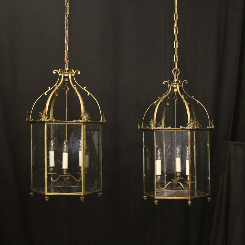 A pair of antique brass hexagonal hall lanterns with glazed glass panels and triple candle-style light fittings suspended from chains.