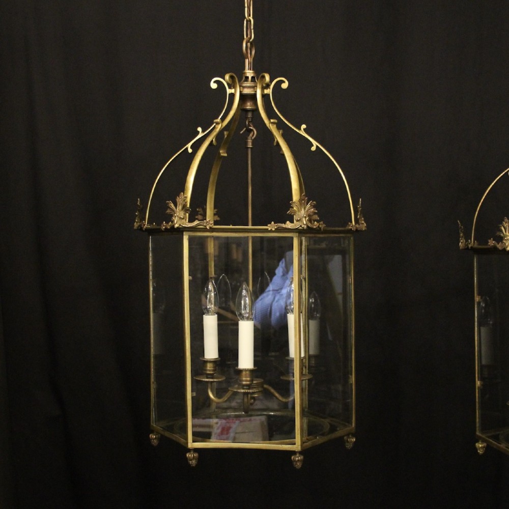 A pair of antique brass hexagonal hall lanterns with glazed glass panels and triple candle-style light fittings suspended from chains. View II
