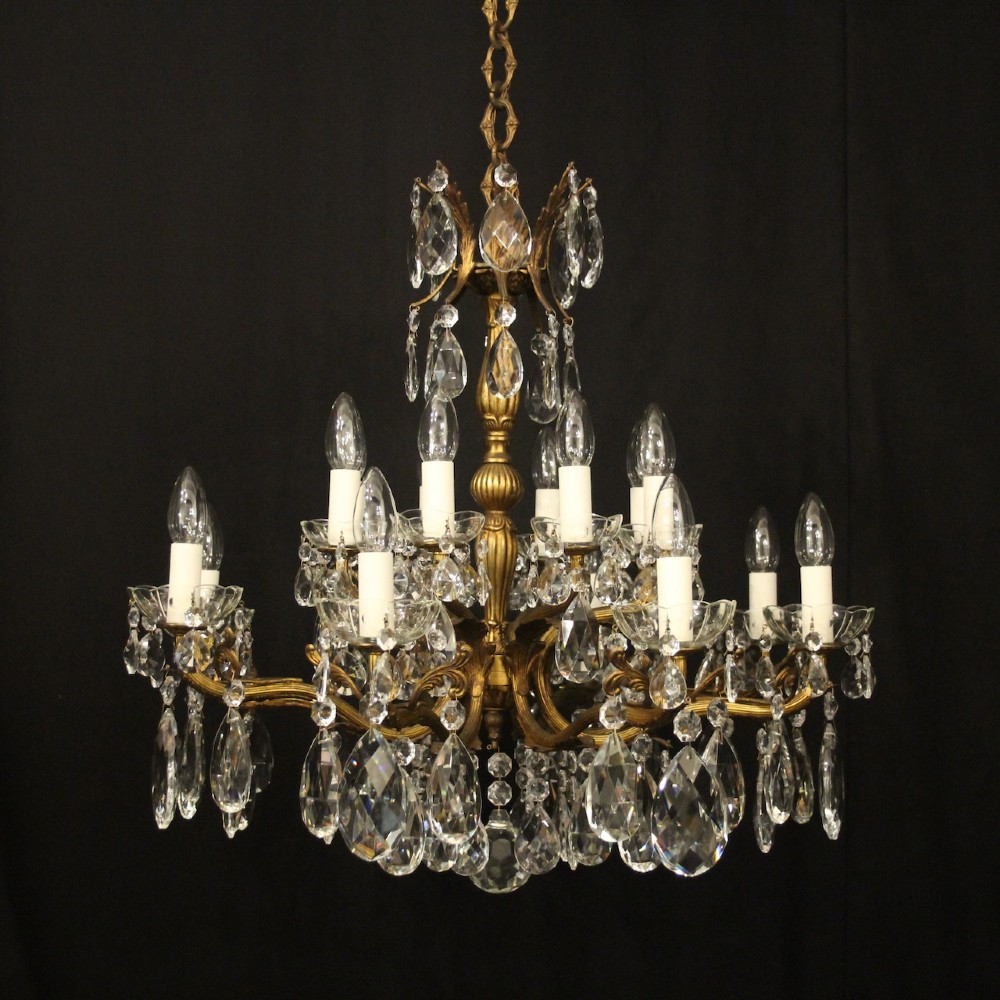 A multi-tiered antique French ceiling chandelier made of gilded brass with sixteen candle-style lights and faceted crystal drops against a dark background.