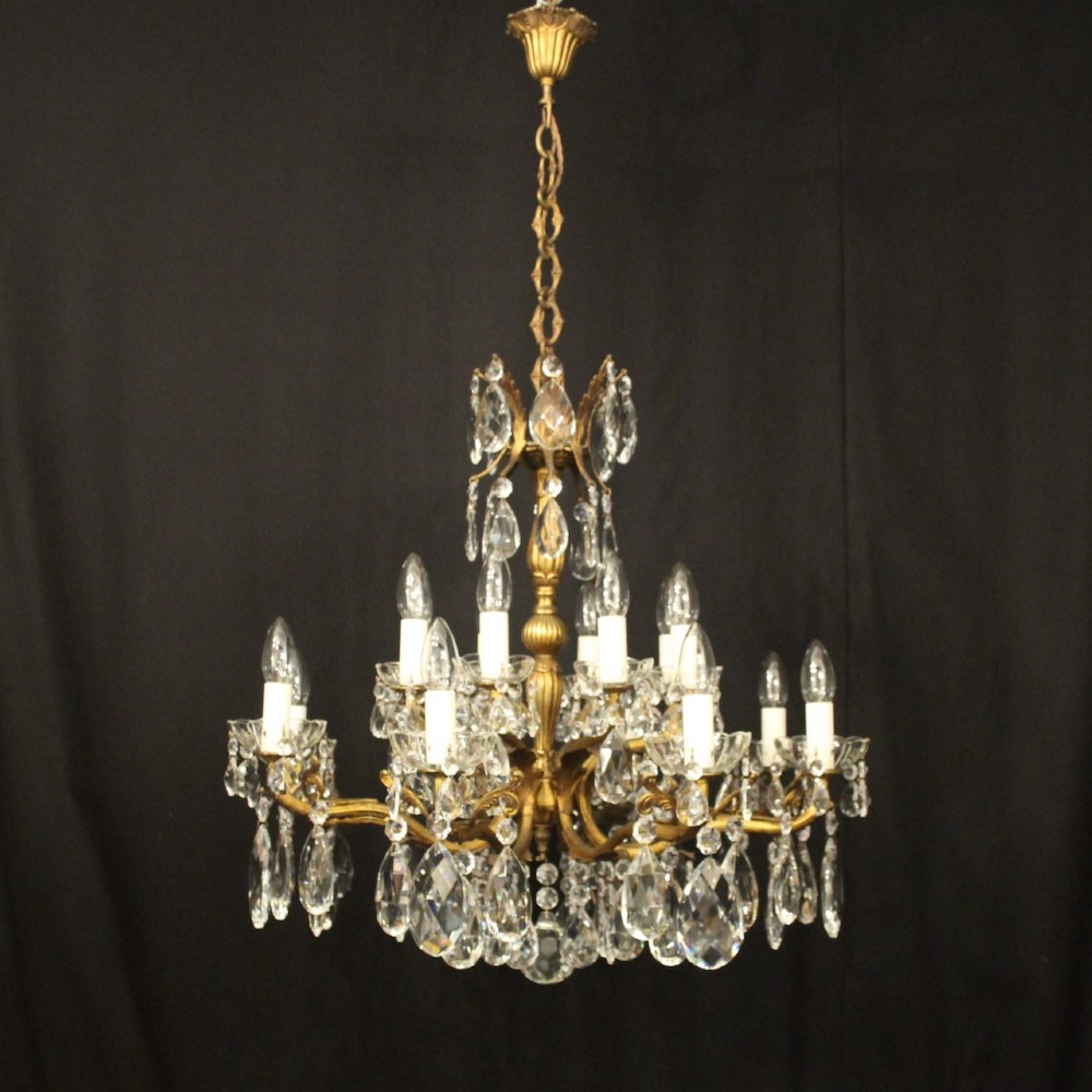 A multi-tiered antique French ceiling chandelier made of gilded brass with sixteen candle-style lights and faceted crystal drops against a dark background. View II