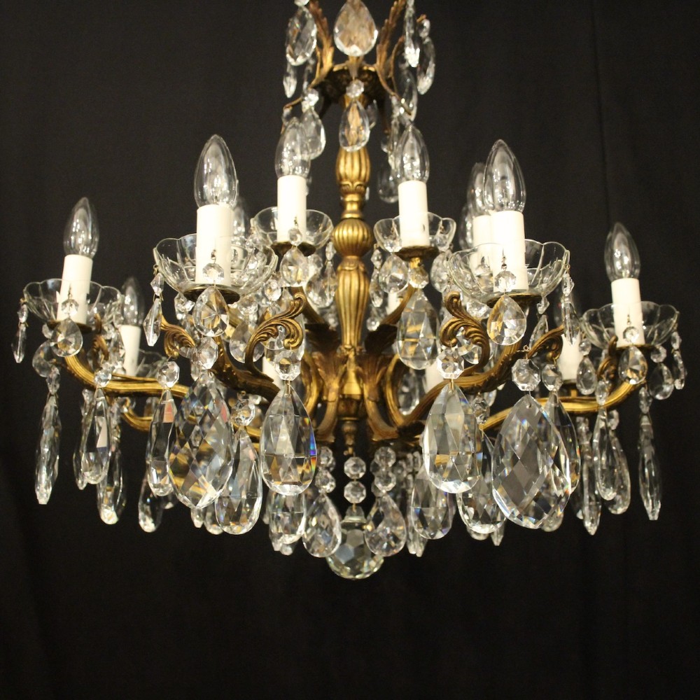 A multi-tiered antique French ceiling chandelier made of gilded brass with sixteen candle-style lights and faceted crystal drops against a dark background. View III