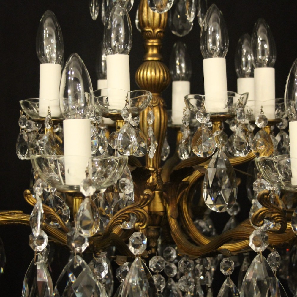 A multi-tiered antique French ceiling chandelier made of gilded brass with sixteen candle-style lights and faceted crystal drops against a dark background. View VII