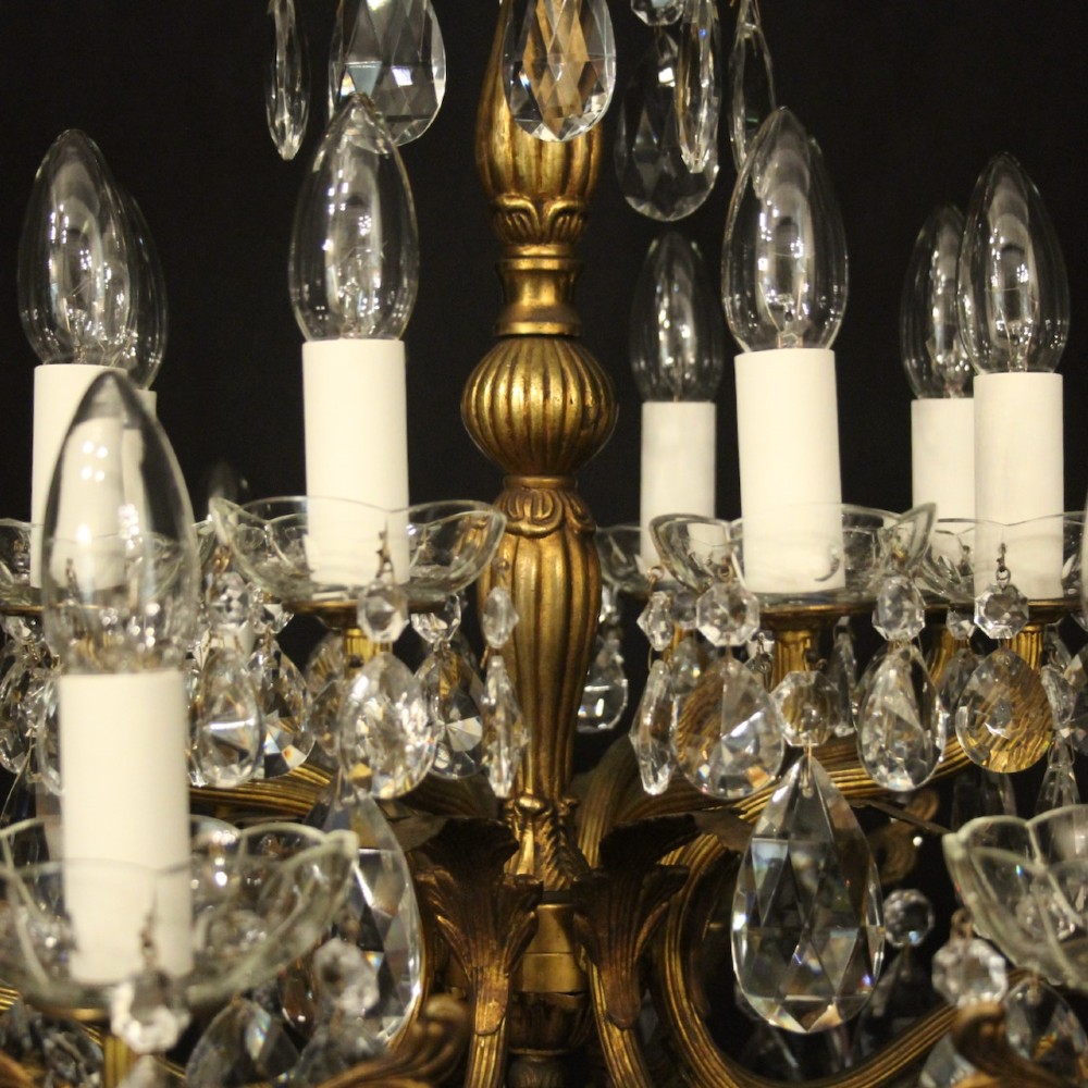 A multi-tiered antique French ceiling chandelier made of gilded brass with sixteen candle-style lights and faceted crystal drops against a dark background. View VIII