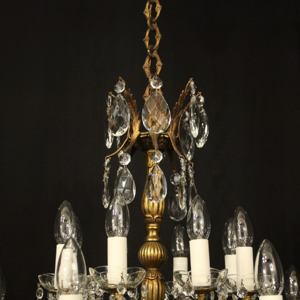 A multi-tiered antique French ceiling chandelier made of gilded brass with sixteen candle-style lights and faceted crystal drops against a dark background. View IX