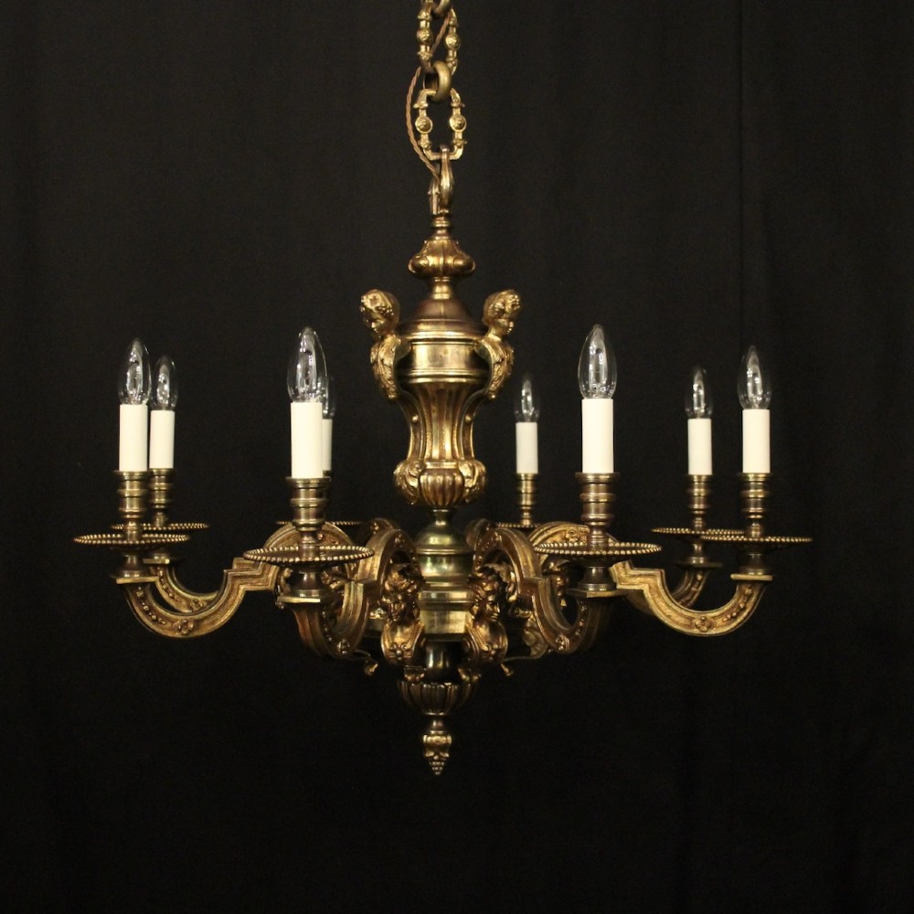 An antique French eight-light chandelier crafted from gilded bronze, featuring sculpted figures, classical motifs, and candle-style bulb holders.