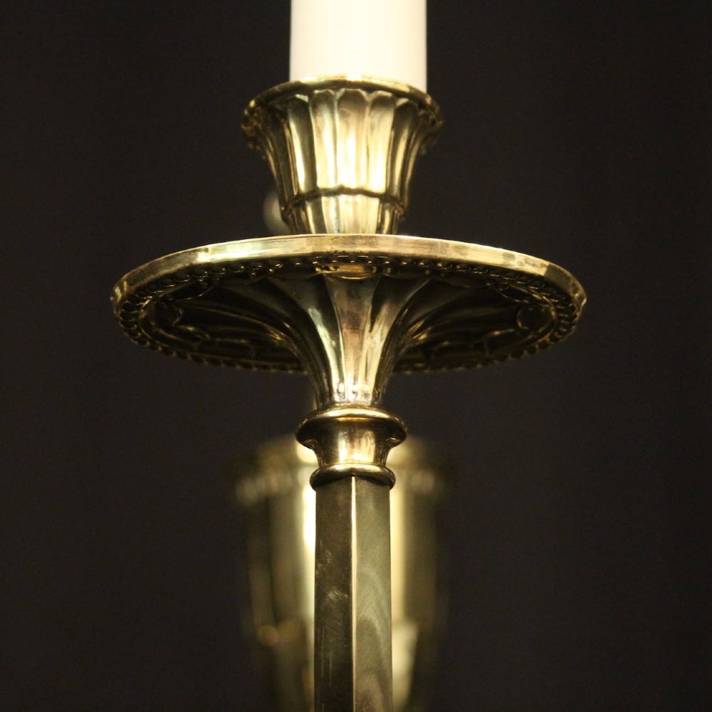 A repolished brass ten-light chandelier featuring sweeping curved arms, candle sleeves, and a central urn-shaped stem hanging from a chain. View VI