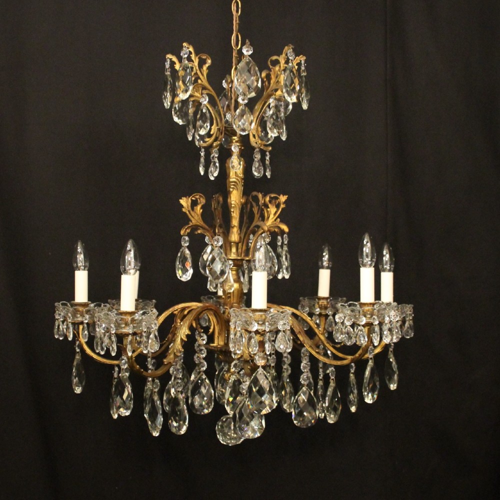 An eight-light French chandelier featuring a gilded metal frame adorned with cut crystal teardrop pendants and glass candle sleeves.
