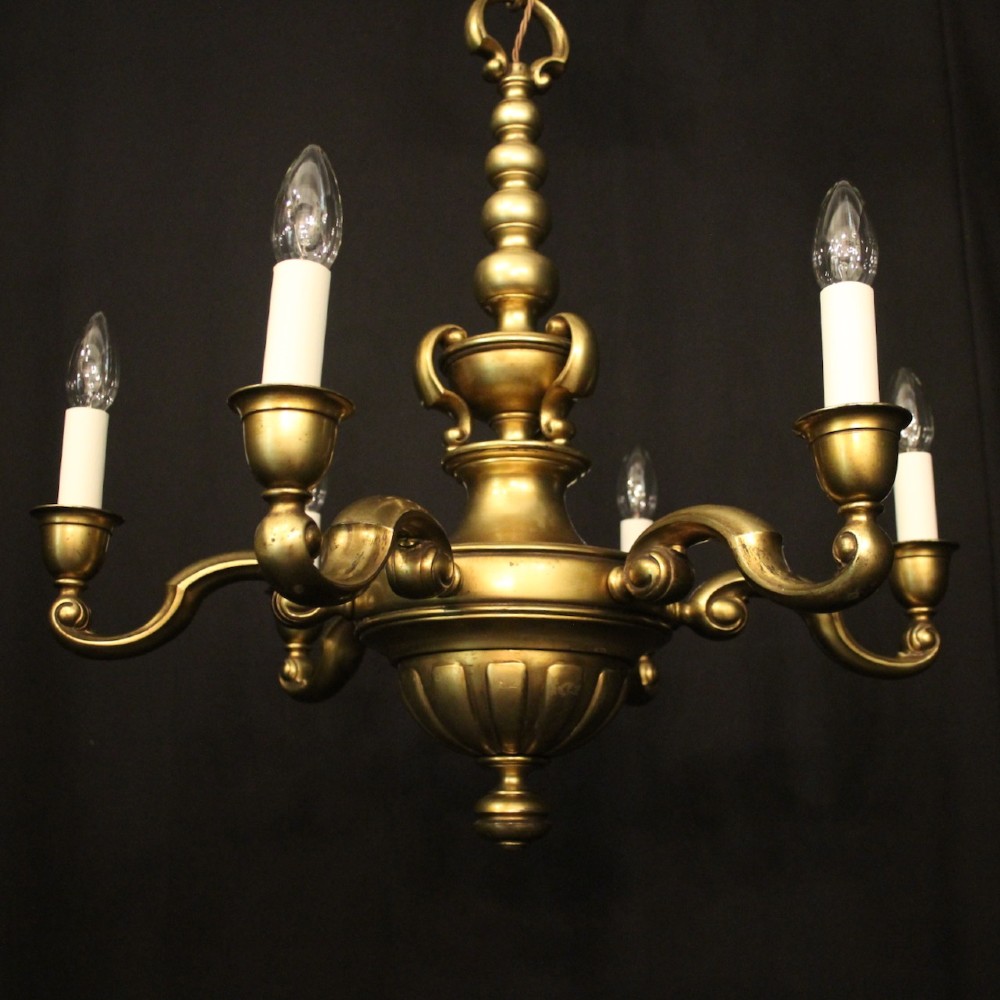 An antique warm brass chandelier featuring six curved scroll arms radiating from a central baluster column with white faux candle sockets. View II
