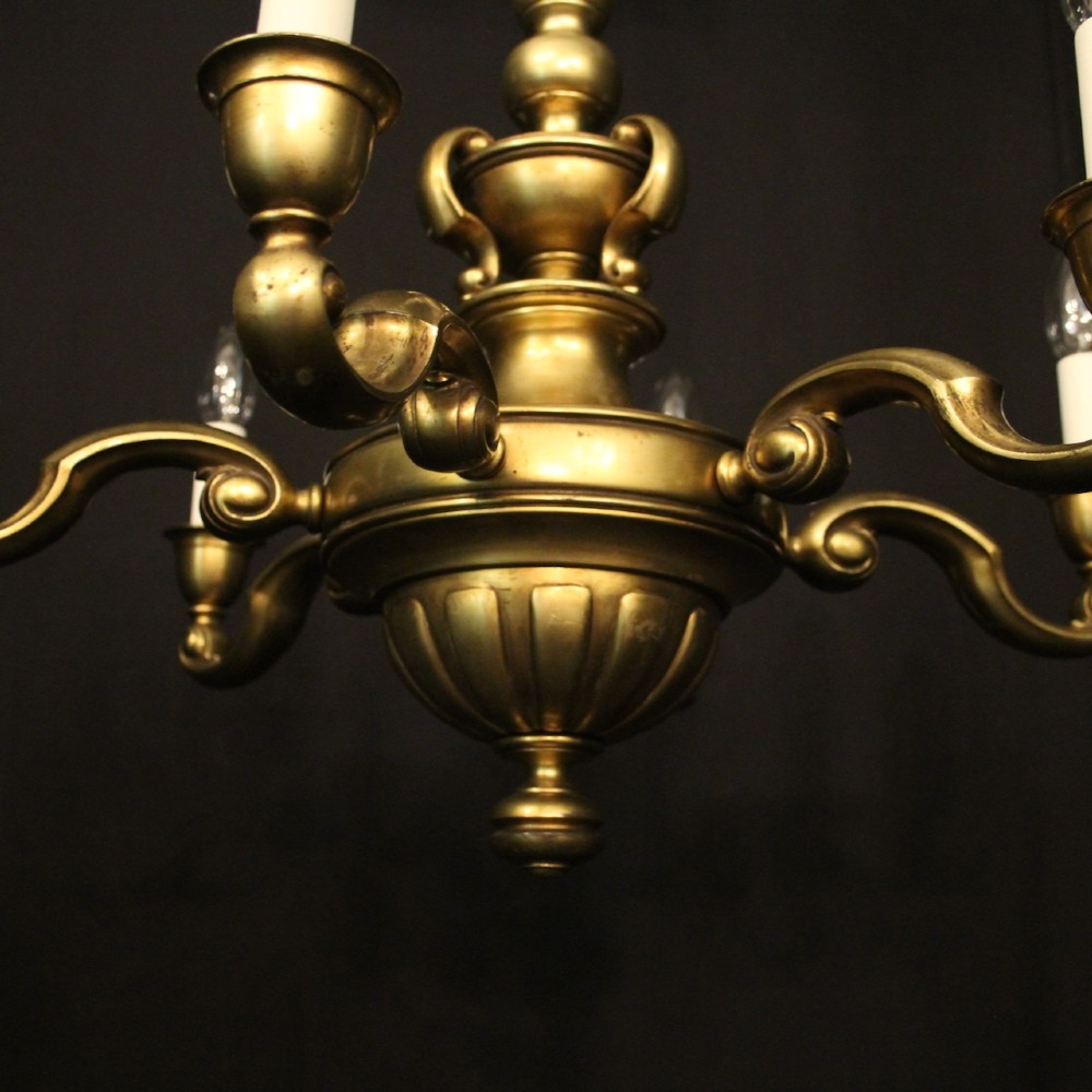 An antique warm brass chandelier featuring six curved scroll arms radiating from a central baluster column with white faux candle sockets. View VII