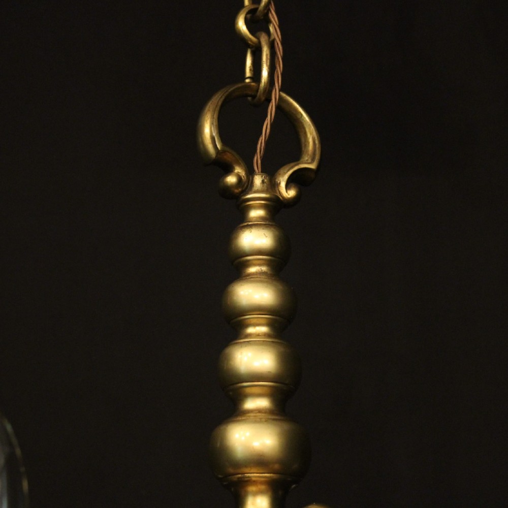 An antique warm brass chandelier featuring six curved scroll arms radiating from a central baluster column with white faux candle sockets. View IX