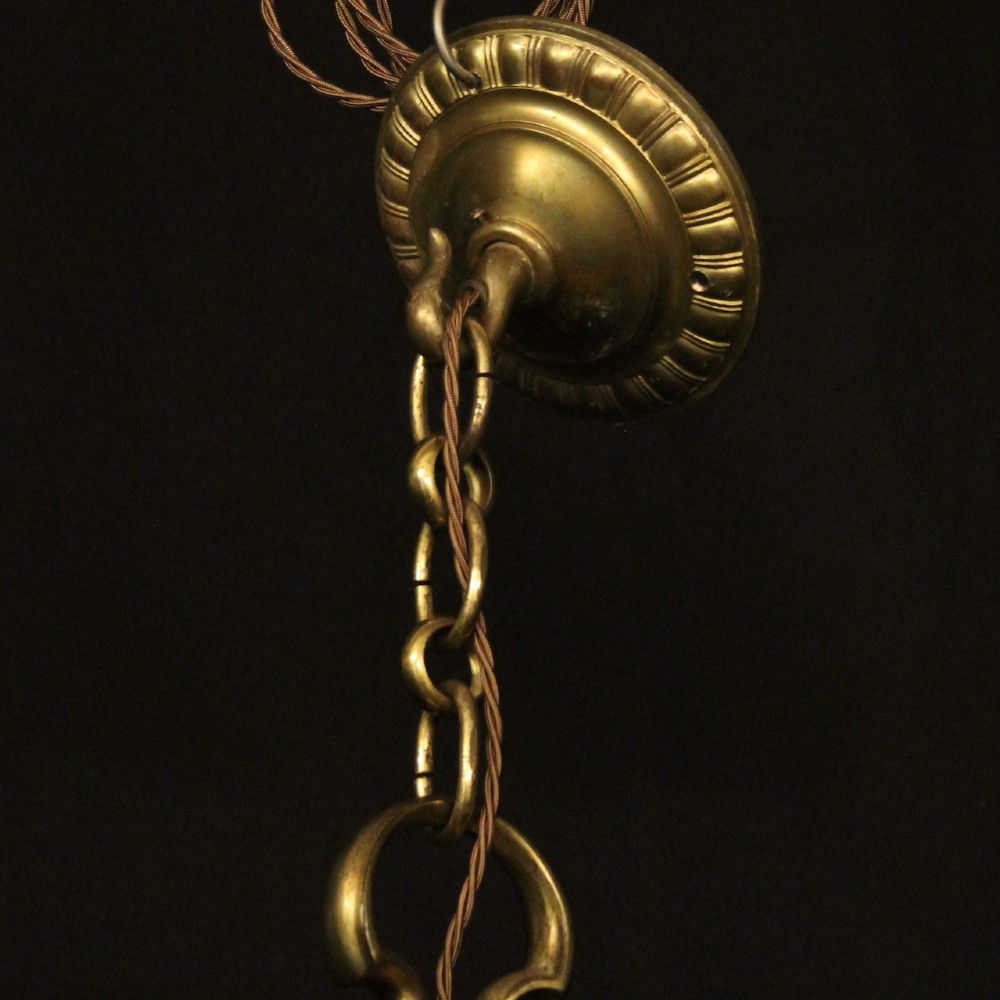 An antique warm brass chandelier featuring six curved scroll arms radiating from a central baluster column with white faux candle sockets. View X