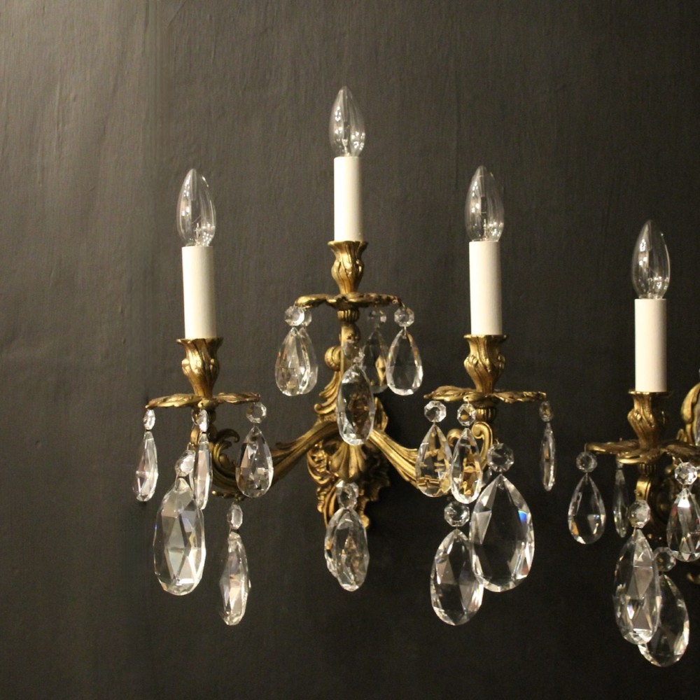 A pair of French three-arm gilded metal wall sconces adorned with hanging clear glass crystal droplets and white candle sleeves. View II