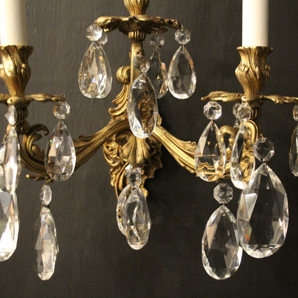 A pair of French three-arm gilded metal wall sconces adorned with hanging clear glass crystal droplets and white candle sleeves. View III