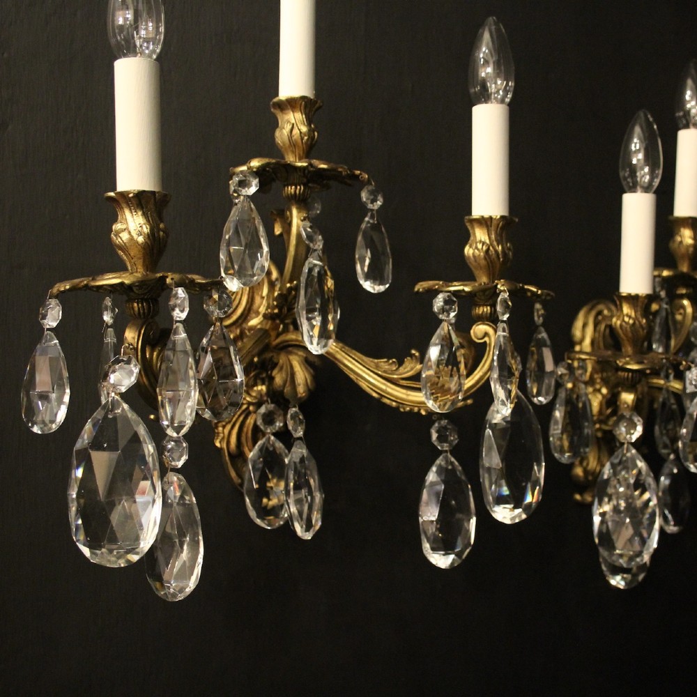 A pair of French three-arm gilded metal wall sconces adorned with hanging clear glass crystal droplets and white candle sleeves. View IV