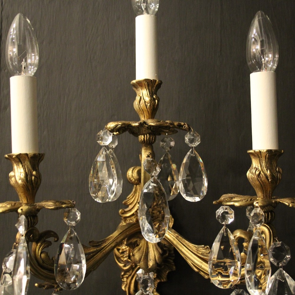 A pair of French three-arm gilded metal wall sconces adorned with hanging clear glass crystal droplets and white candle sleeves. View V