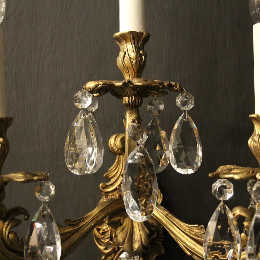 A pair of French three-arm gilded metal wall sconces adorned with hanging clear glass crystal droplets and white candle sleeves. View VI