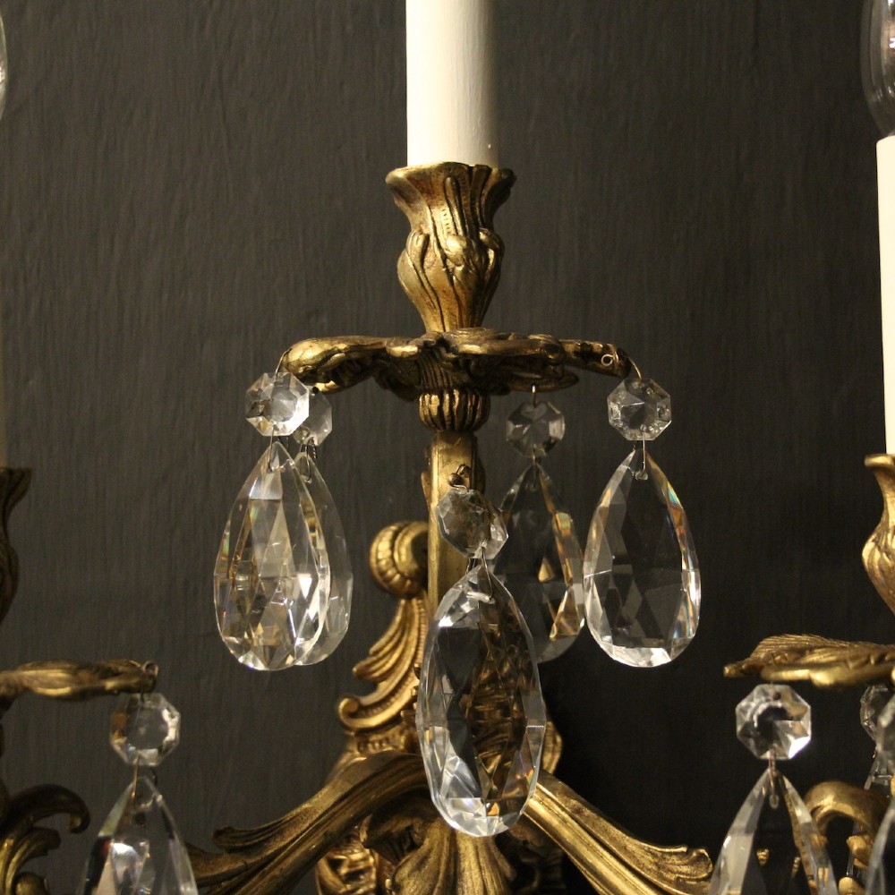 A pair of French three-arm gilded metal wall sconces adorned with hanging clear glass crystal droplets and white candle sleeves. View VII