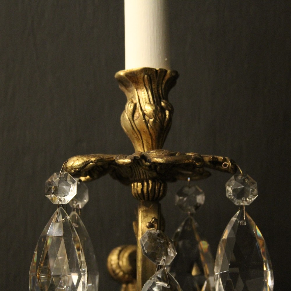 A pair of French three-arm gilded metal wall sconces adorned with hanging clear glass crystal droplets and white candle sleeves. View VIII