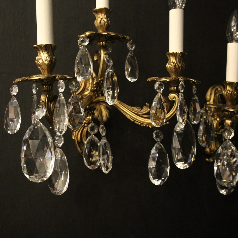 A pair of French three-arm gilded metal wall sconces adorned with hanging clear glass crystal droplets and white candle sleeves. View IX