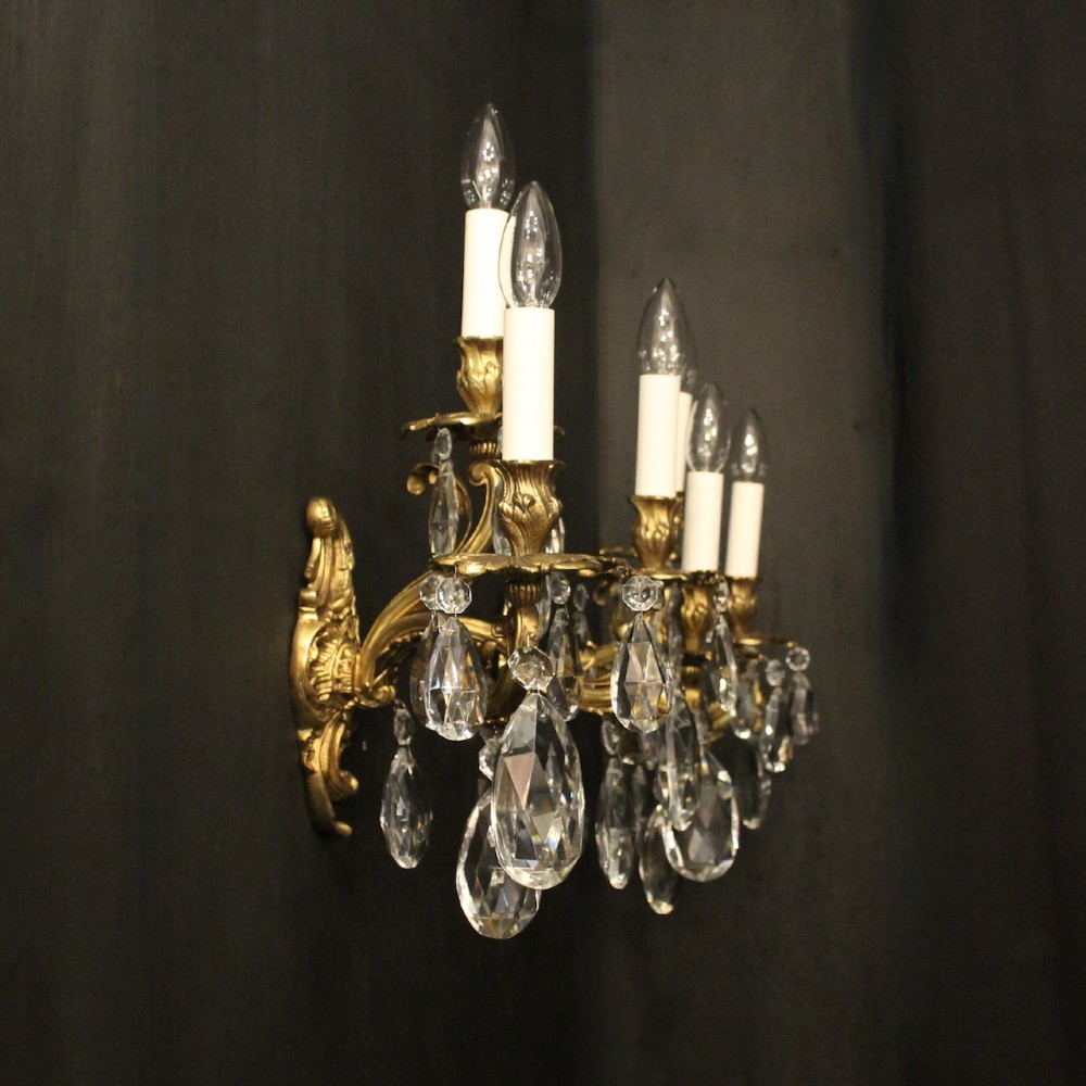 A pair of French three-arm gilded metal wall sconces adorned with hanging clear glass crystal droplets and white candle sleeves. View X