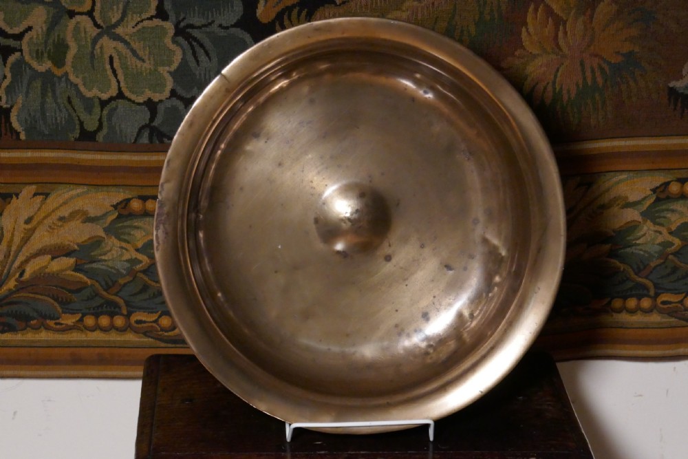 A circular 16th century bronze bowl featuring a broad flat rim and a raised central boss.