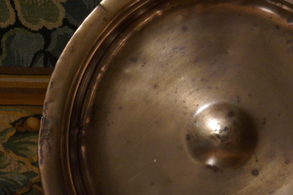 A circular 16th century bronze bowl featuring a broad flat rim and a raised central boss. View II