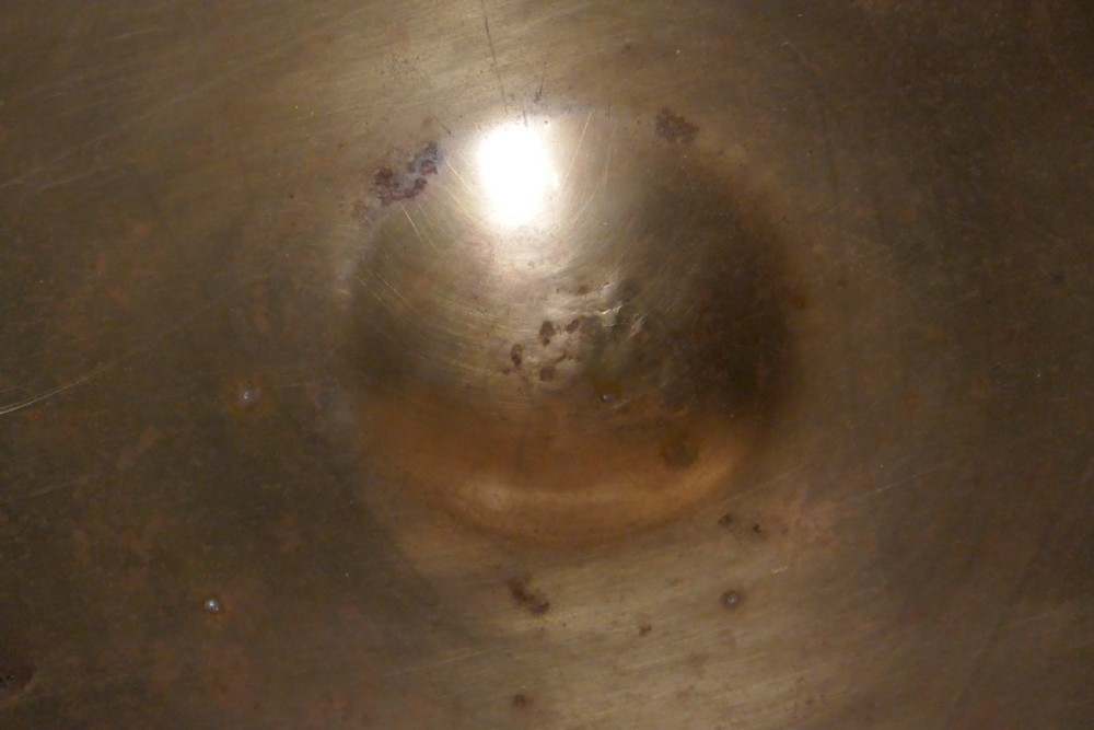 A circular 16th century bronze bowl featuring a broad flat rim and a raised central boss. View III