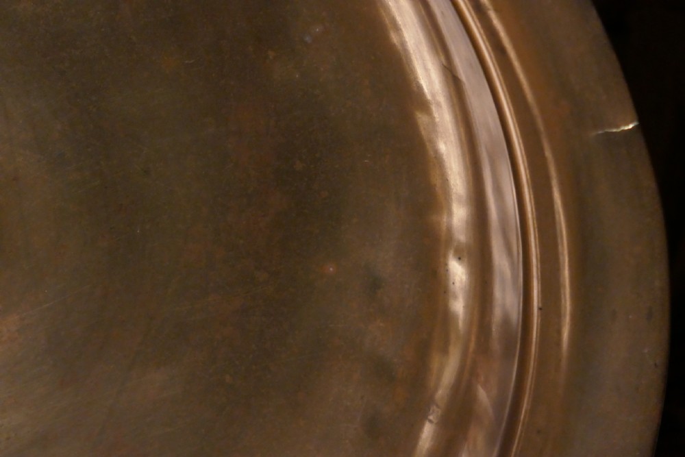 A circular 16th century bronze bowl featuring a broad flat rim and a raised central boss. View IV