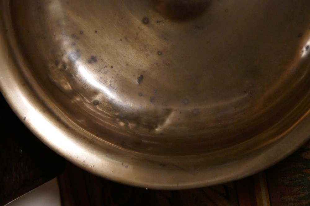 A circular 16th century bronze bowl featuring a broad flat rim and a raised central boss. View VIII