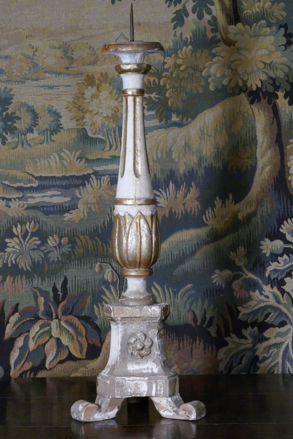 A carved 19th-century wooden pricket candlestick featuring distressed off-white paint, exposed gold leafing, an acanthus column motif, and an iron candle spike.