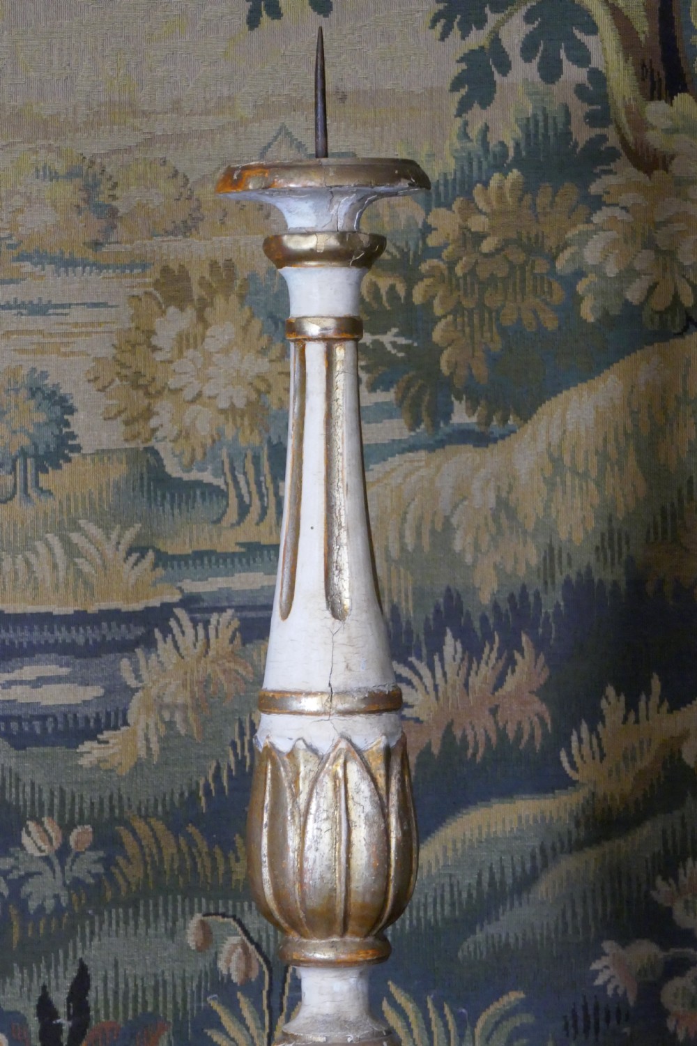 A carved 19th-century wooden pricket candlestick featuring distressed off-white paint, exposed gold leafing, an acanthus column motif, and an iron candle spike. View II